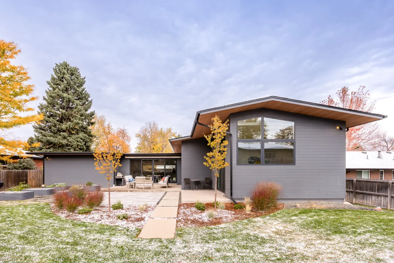 The Centennial Modern Ranch features a gray exterior with a butterfly roof and floor-to-ceiling glazing in the backyard patio area.