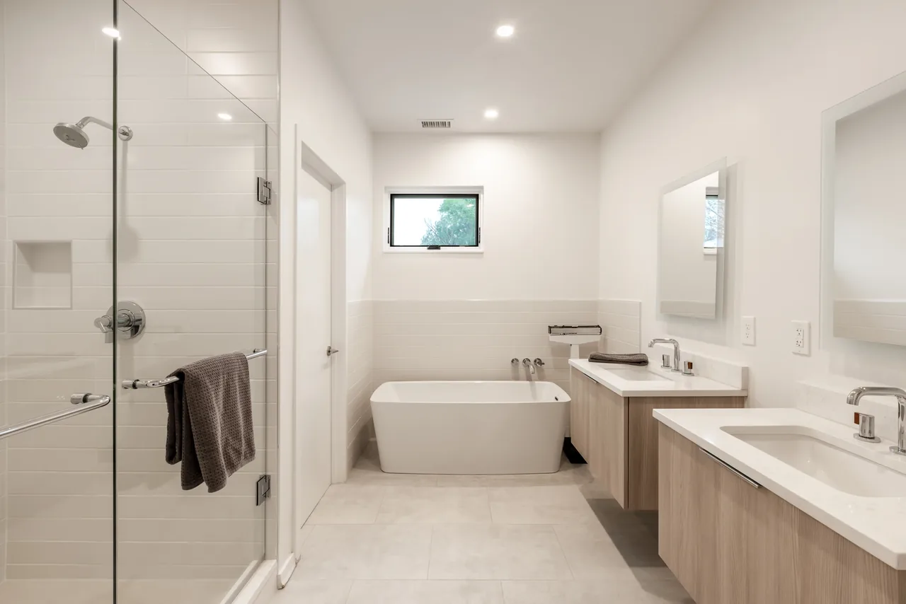 Modern bathroom featuring a freestanding tub, glass shower enclosure, and dual floating vanities under recessed lighting.