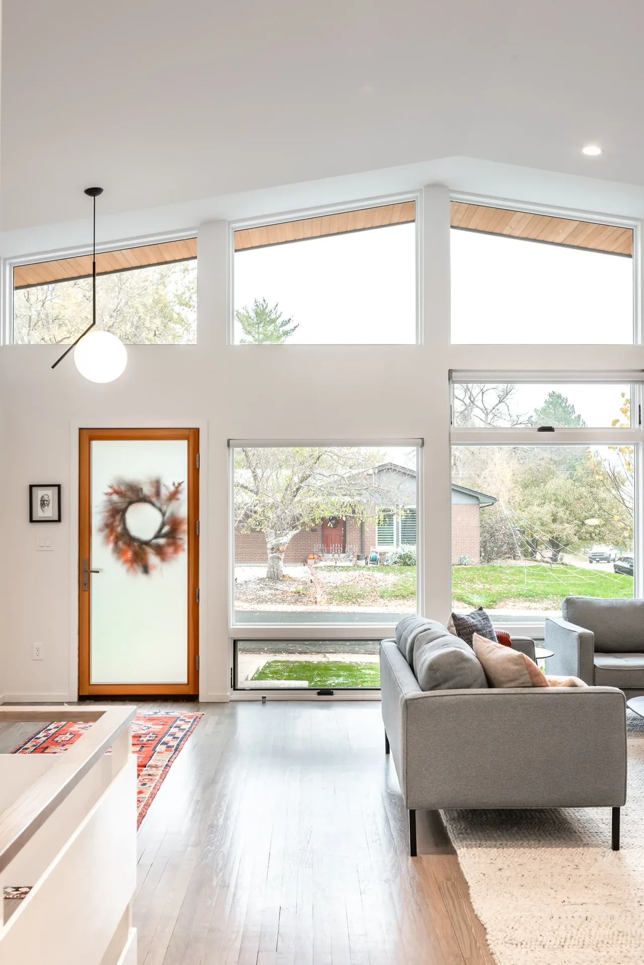 Living area featuring tall windows with wooden sloped roof eaves visible outside and a frosted glass door accented with a wreath.