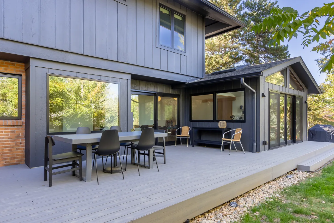 Rear exterior view of a two-story house featuring a spacious deck with an outdoor dining table and multiple seating areas.