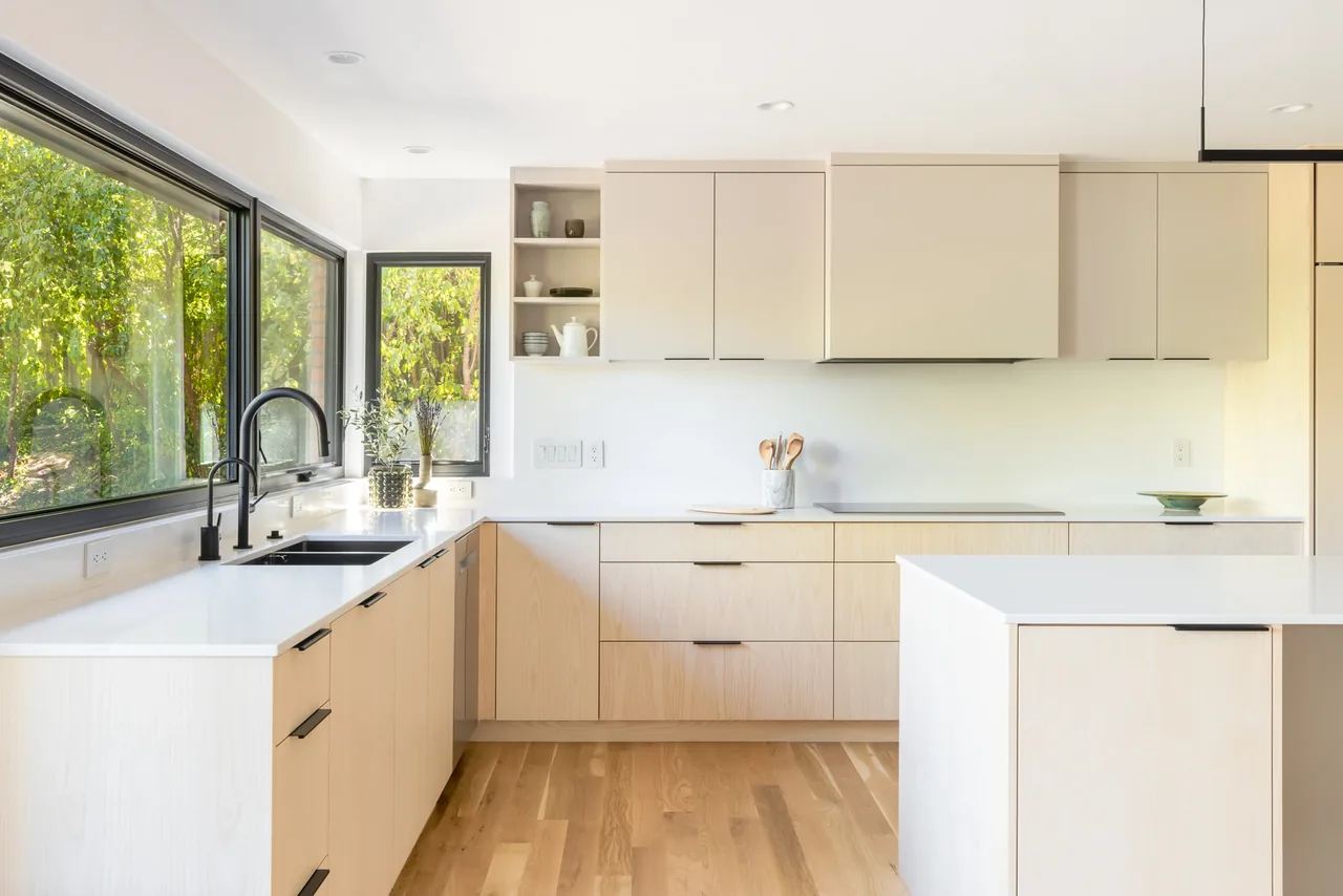 Kitchen interior featuring a light wood island, undermount sink, and floor-to-ceiling glazing windows.