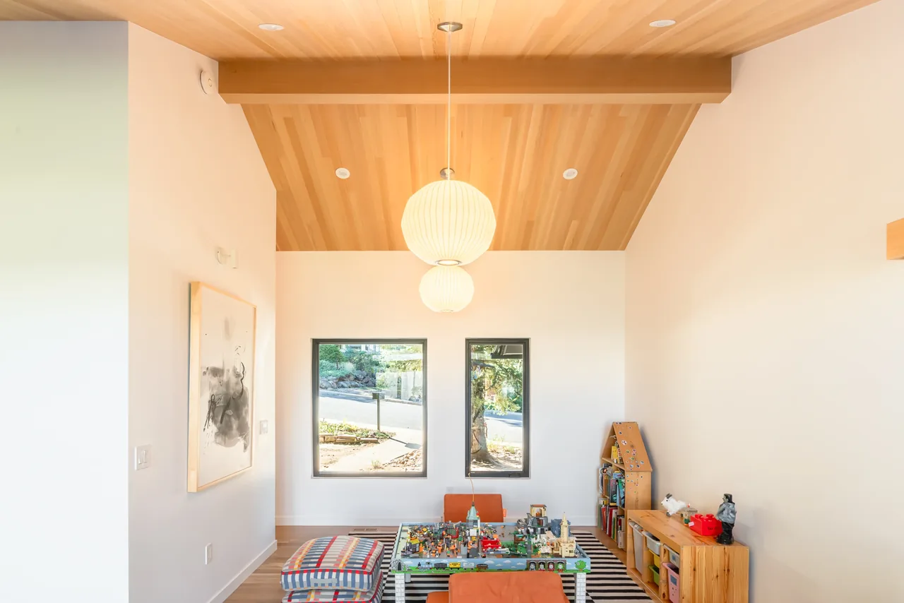 A small playroom features a wood-paneled vaulted ceiling, two rectangular windows, and organized toy storage along one wall.