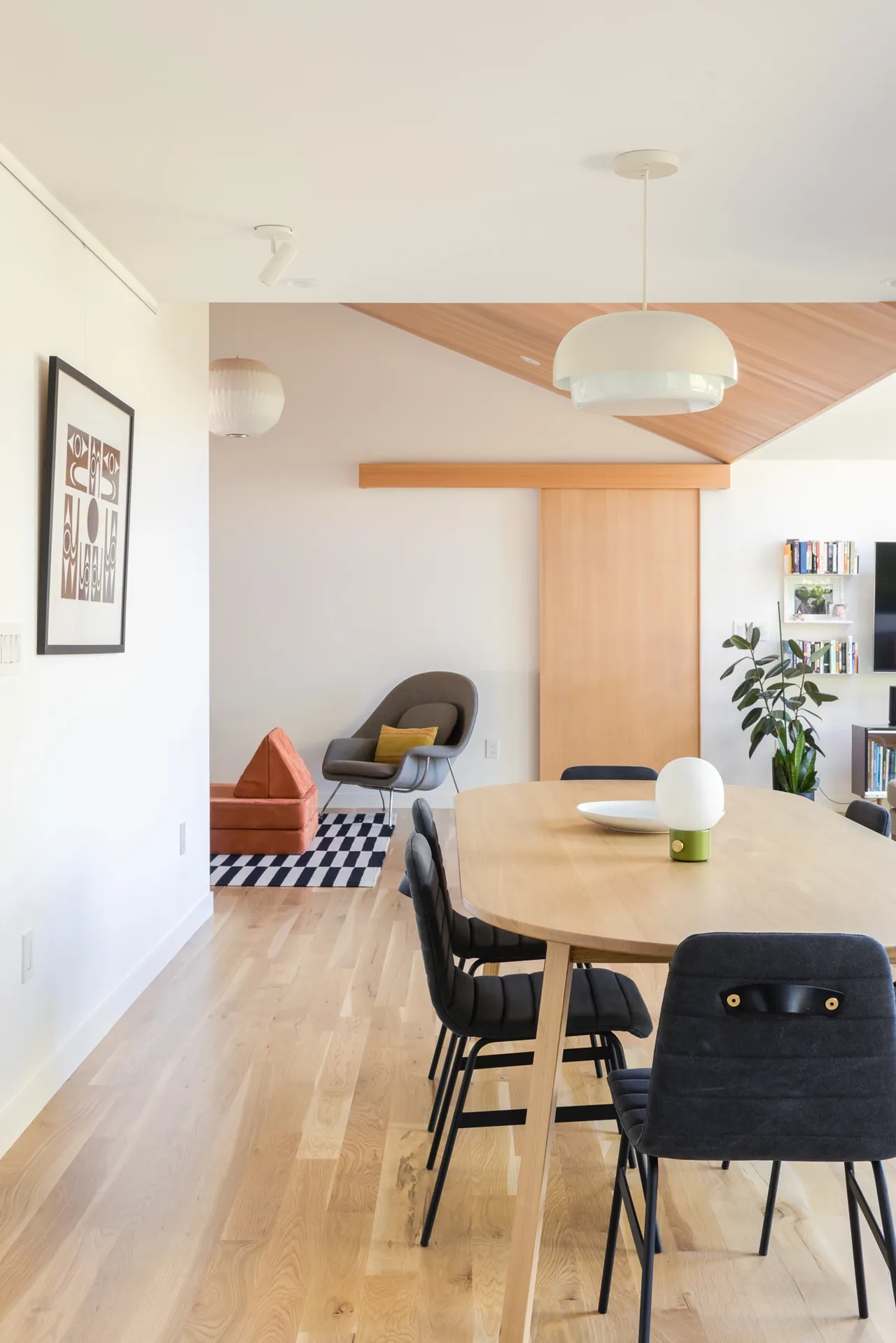 Dining area with wooden table and black chairs, modern white pendant light, and adjacent seating area with an armchair and ottoman.