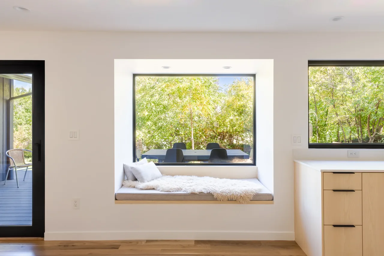 Built-in window seat with cushions between two large windows in a modern kitchen space.