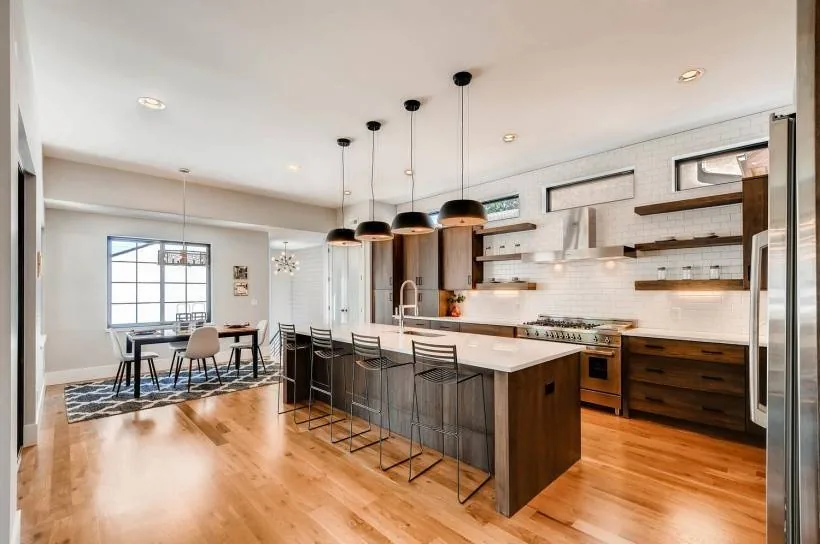 Open plan kitchen and dining room with wood flooring, island with pendant lighting, and large windows.