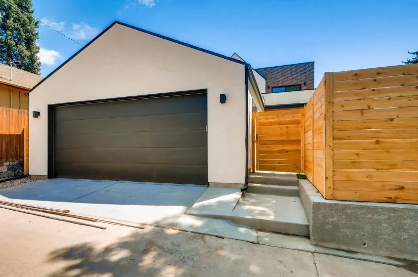 View of a detached garage with stucco exterior, pitched roof, and adjacent wooden fence and steps.