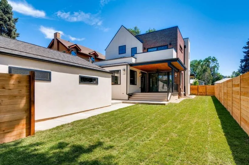 Rear exterior view of a modern modern brick and stucco house with pitched roof and covered patio.