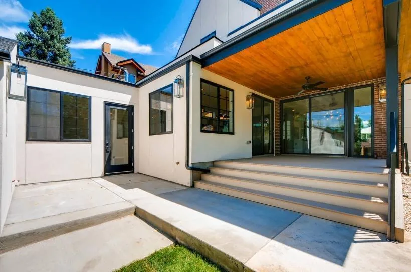 Covered patio area with wood ceiling and concrete steps at the rear of a modern house featuring brick and stucco facades.