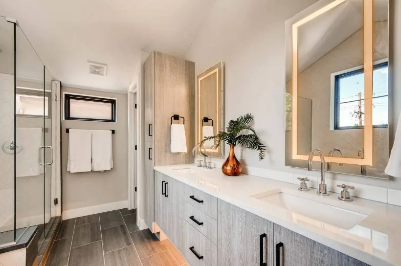Bathroom with wood-effect cabinets, double under-mount sinks, and a walk-in shower with glass enclosure and dark tile floor.
