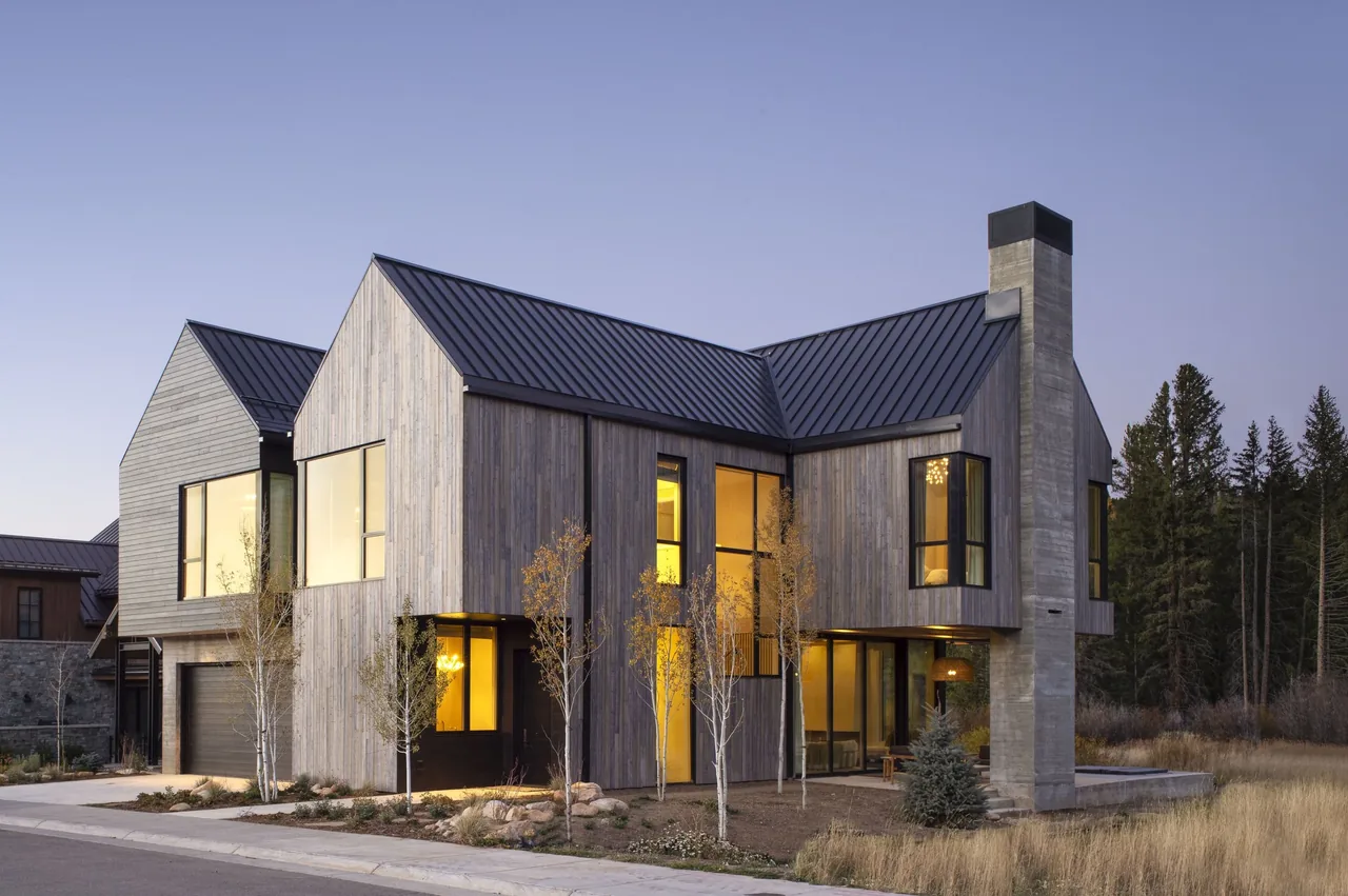 Two-story modern house with vertical wood siding, large corner windows, and a metal gable roof at dusk.