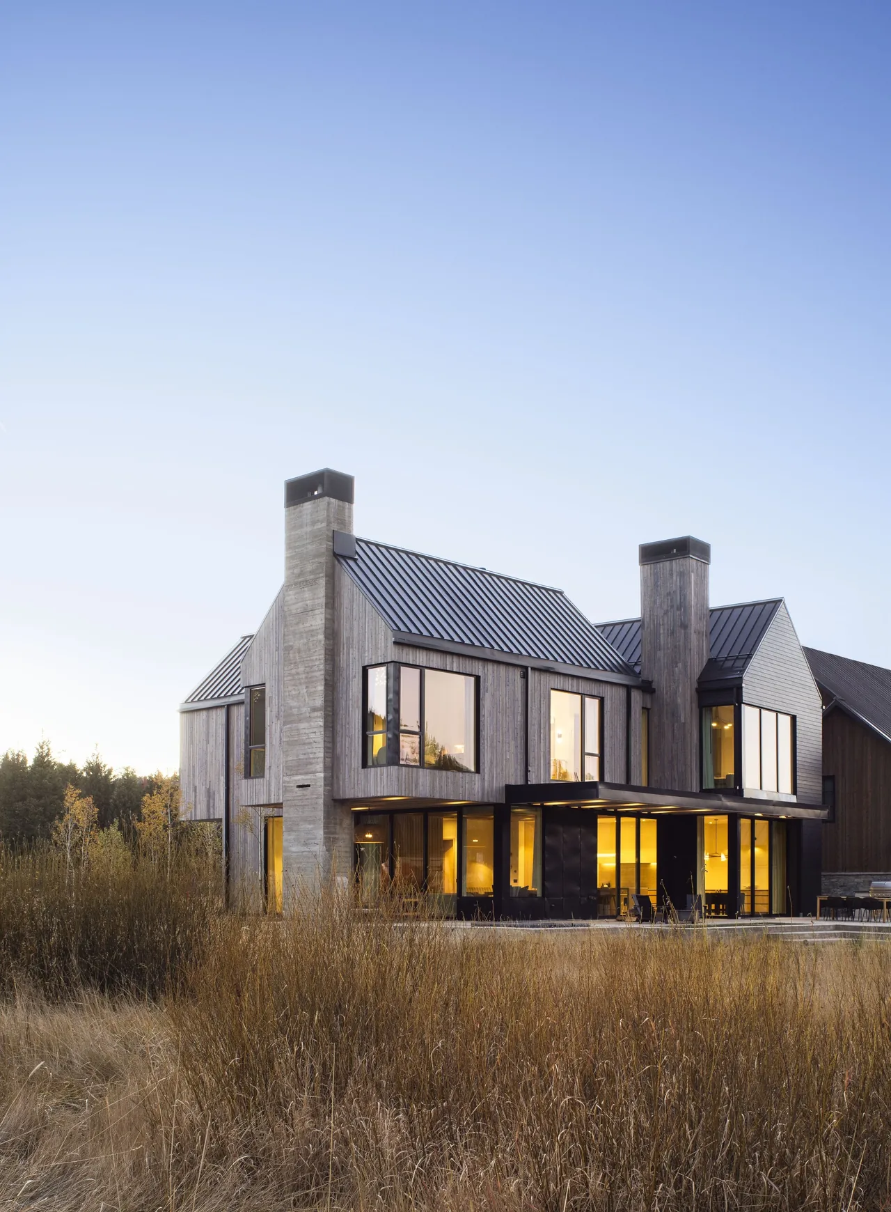 Winter Park residence shows vertical wood siding, concrete chimneys, gable metal roofs, and large corner windows with floor-to-ceiling glazing.