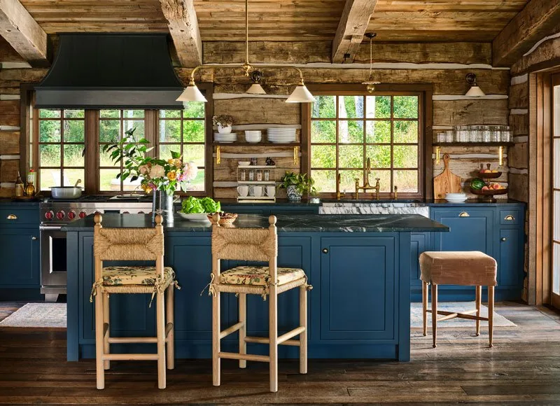 The kitchen in Strawberry Park Homestead features exposed wood beams, blue cabinetry, and open shelving against a log cabin wall.