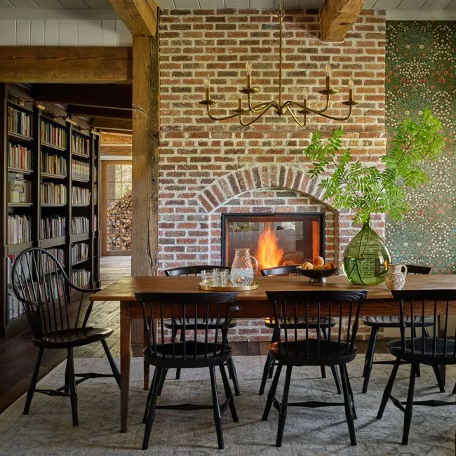 Dining area featuring a brick fireplace with arched detail, black Windsor chairs, and a brass chandelier in the Strawberry Park Homestead.