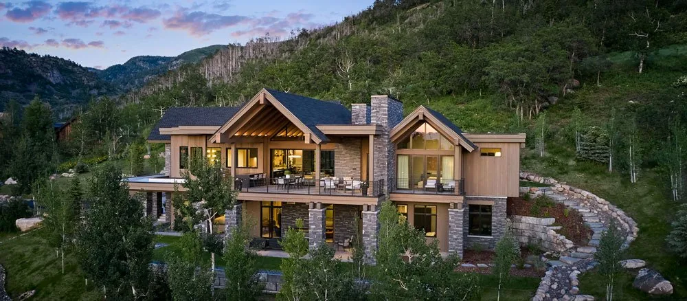 Meadow Mountain Retreat features a modern home combining stone and wood materials with large pitched roofs and multiple outdoor patios.