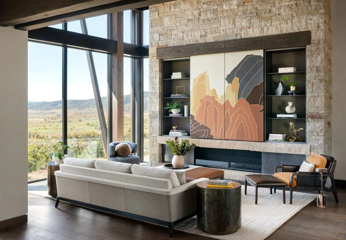 Living room interior with floor-to-ceiling windows and a stone fireplace with built-in shelving.