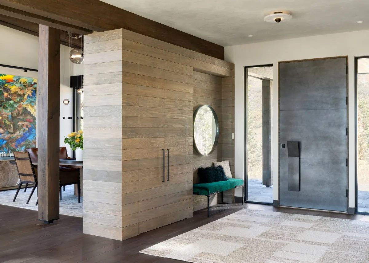 Entry view showing large metal pivot door, glass sidelights, wood wall paneling, and built-in bench.