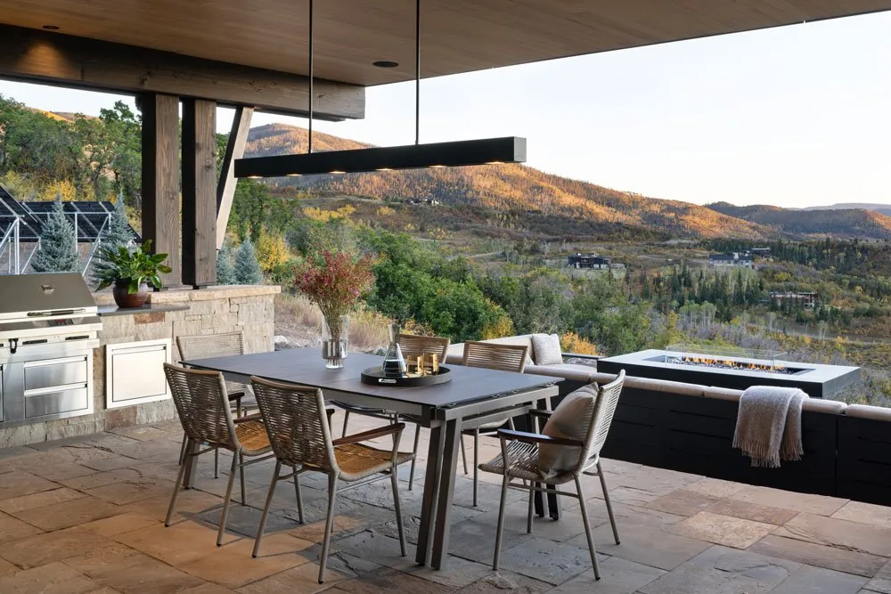 Covered patio with outdoor dining furniture and built-in grill overlooking wooded hills.