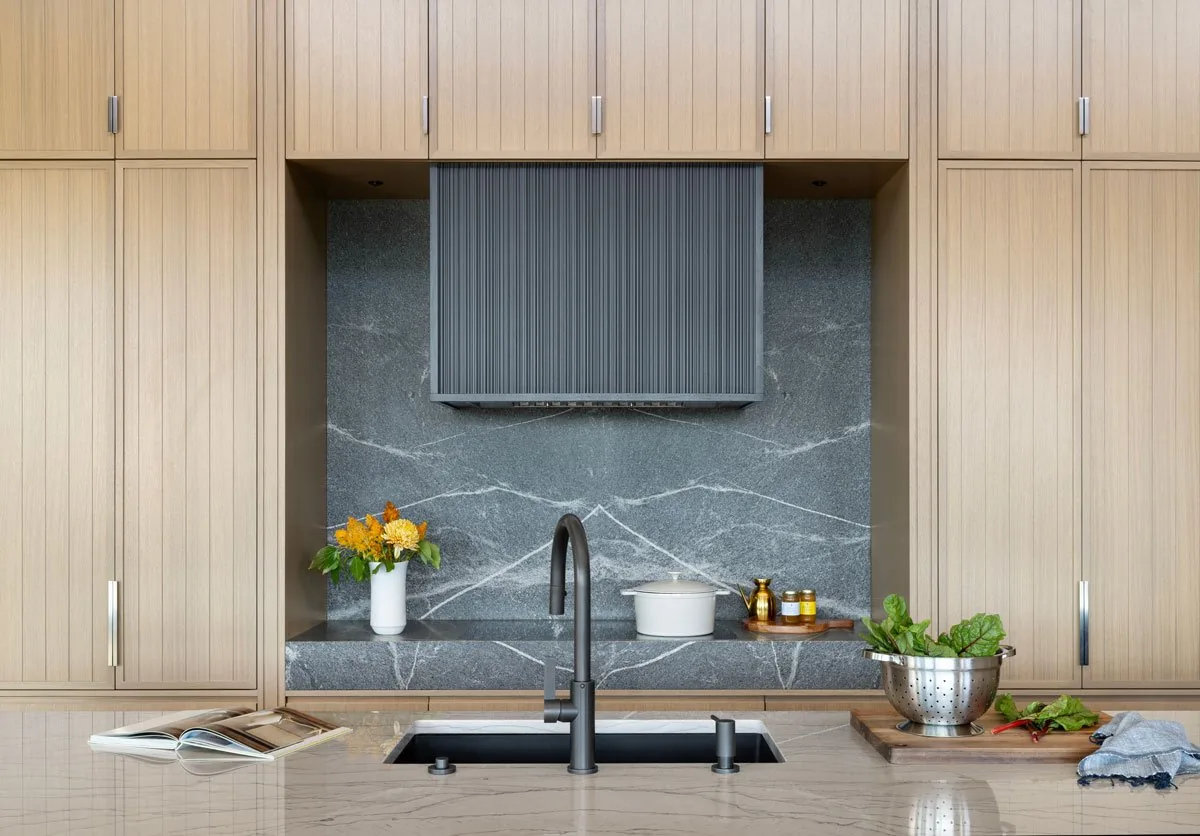 Kitchen interior featuring wood cabinets, dark stone backsplash and countertop, and black faucet on island.