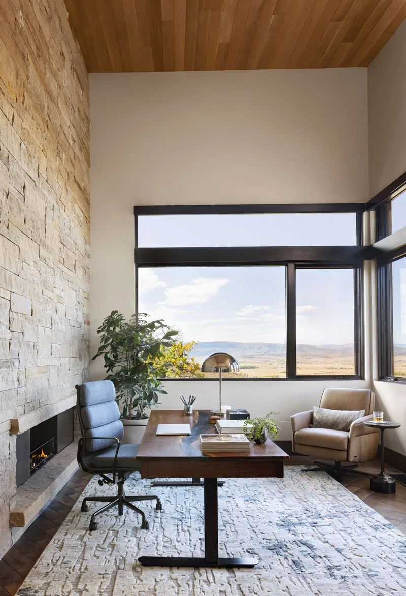 Office space featuring a stone fireplace, wood ceiling, and large corner windows with landscape views.
