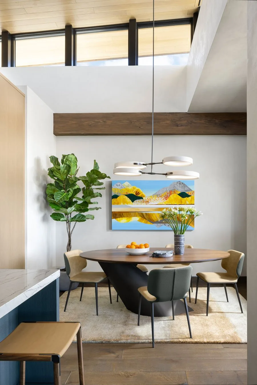 Dining area featuring an oval wooden table with six chairs, a large green plant, a colorful abstract painting, and a modern circular pendant light.
