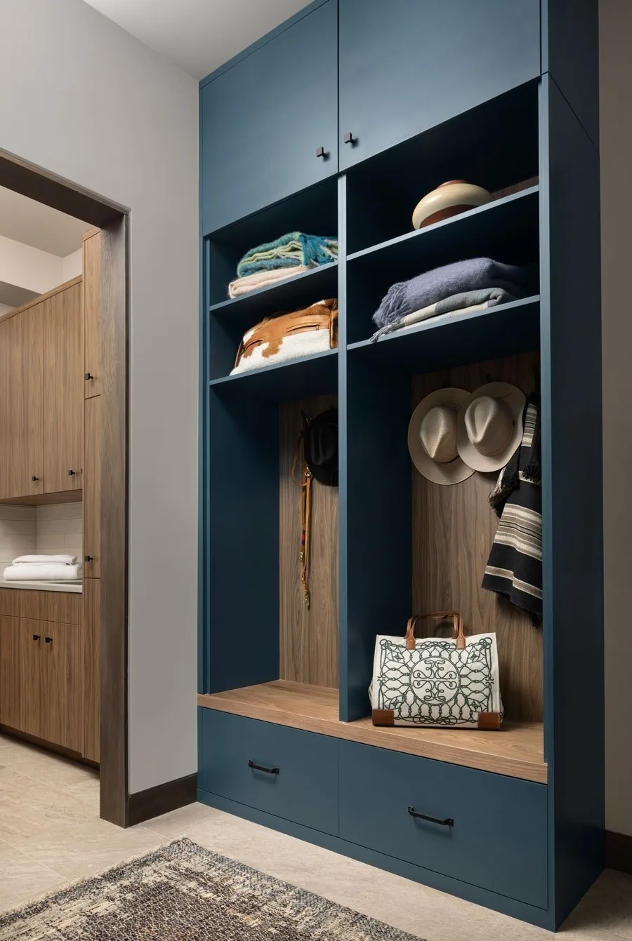 Built-in blue cubby cabinetry in a mudroom with wooden back paneling and adjacent wood cabinetry is shown.