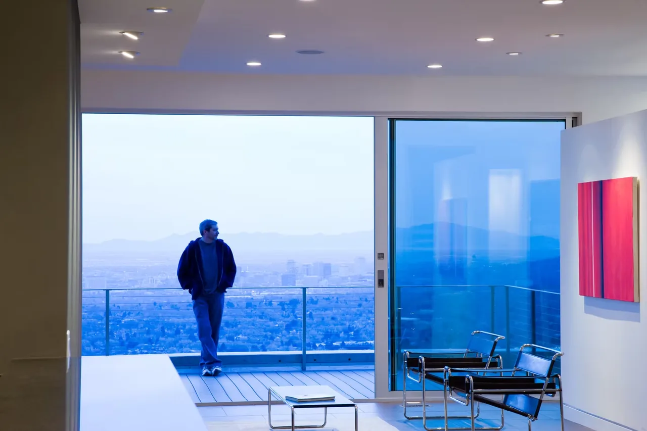 View from a modern interior room onto an outdoor balcony with floor-to-ceiling glazing and a city view.