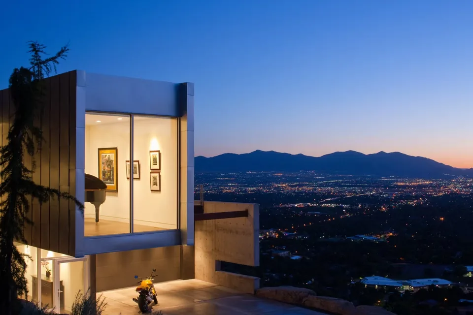 Cantilevered upper level with floor-to-ceiling glass walls in a modern steel and concrete house at dusk