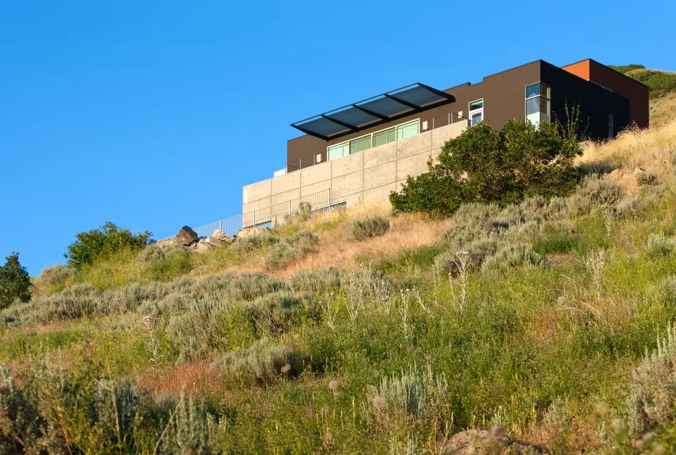 Modern hillside house with flat roof, concrete and steel exterior, and floor-to-ceiling glazing.