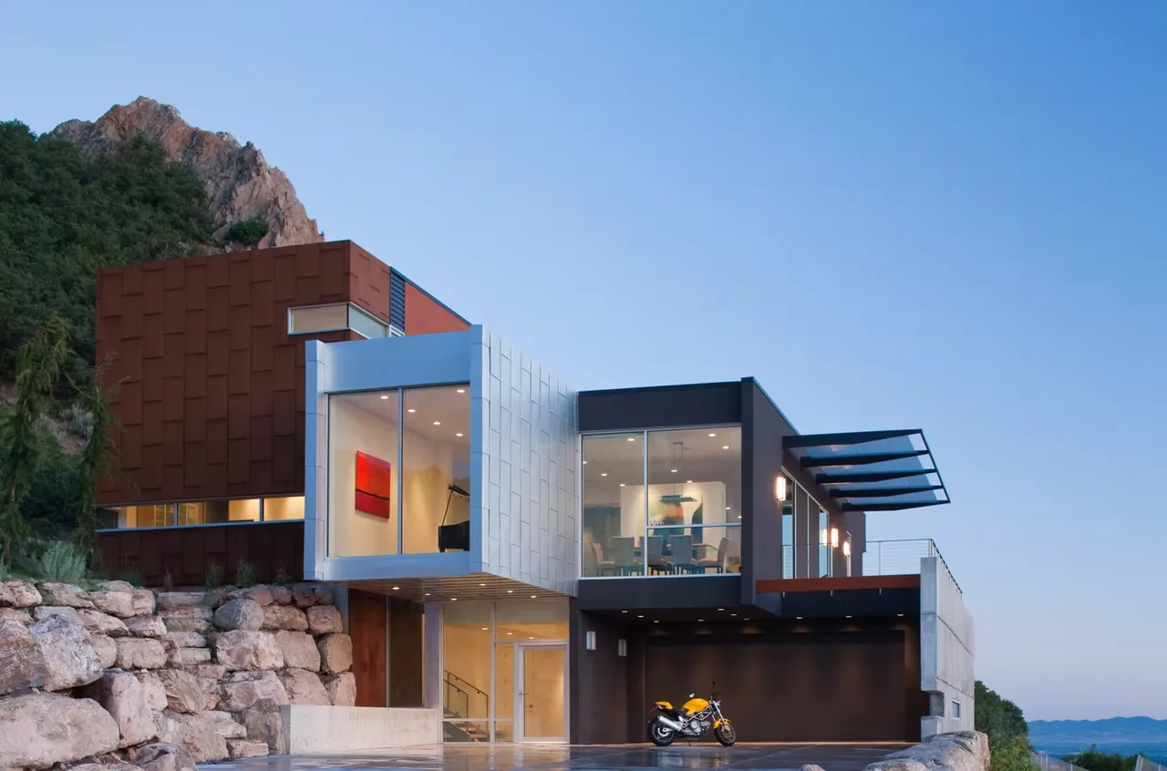 Modern house featuring cantilevered upper floors, floor-to-ceiling glazing, and a flat roof on a rocky site.