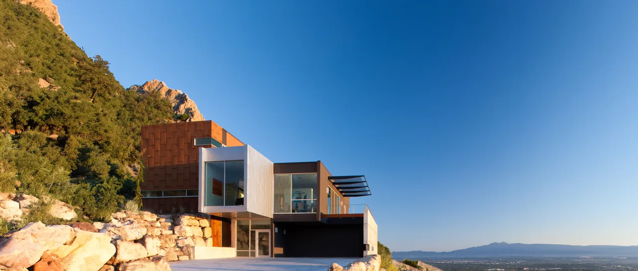 View of H-House showing multiple materials and large windows on a rocky site.