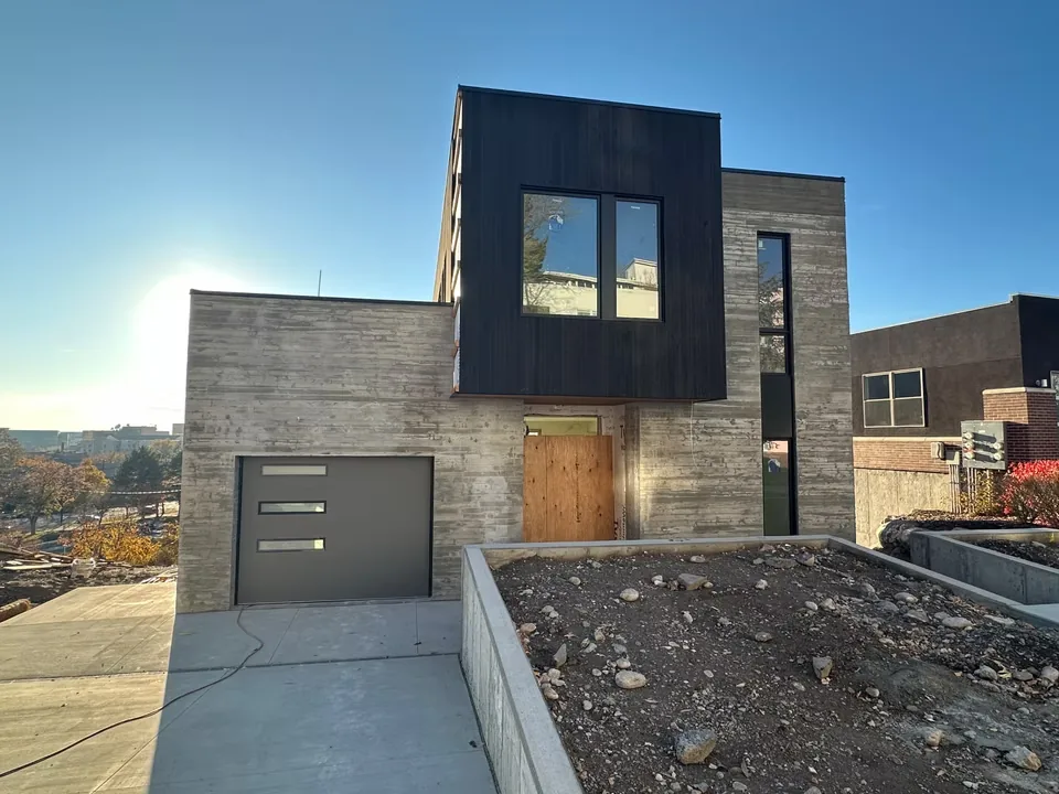 Exterior front view of a modern house featuring board-formed concrete and dark wood cladding with flat roof design and rectangular windows.