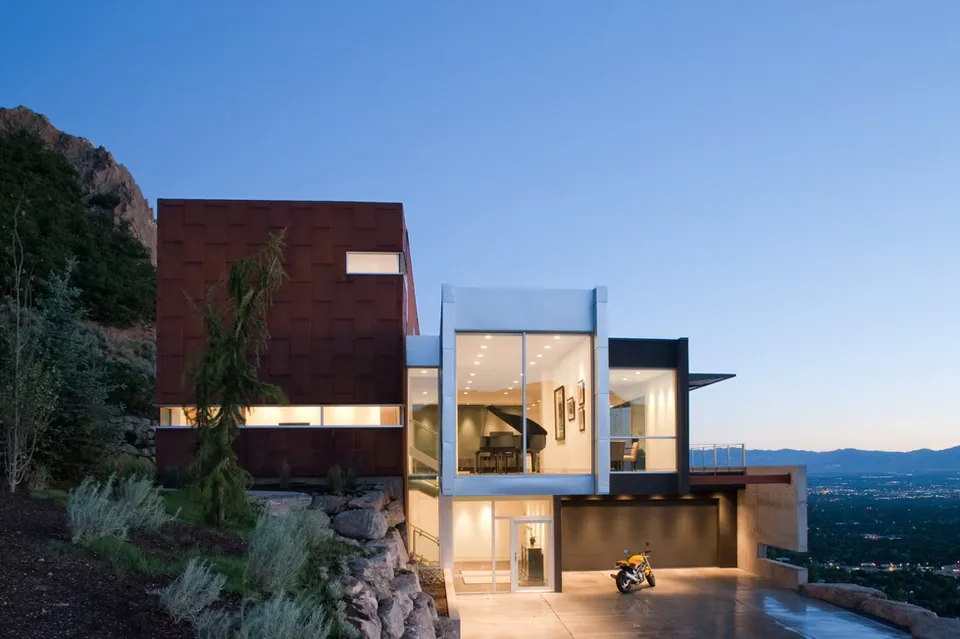 Exterior front view of a modern cantilevered house with large glass panels and a flat roof at dusk.