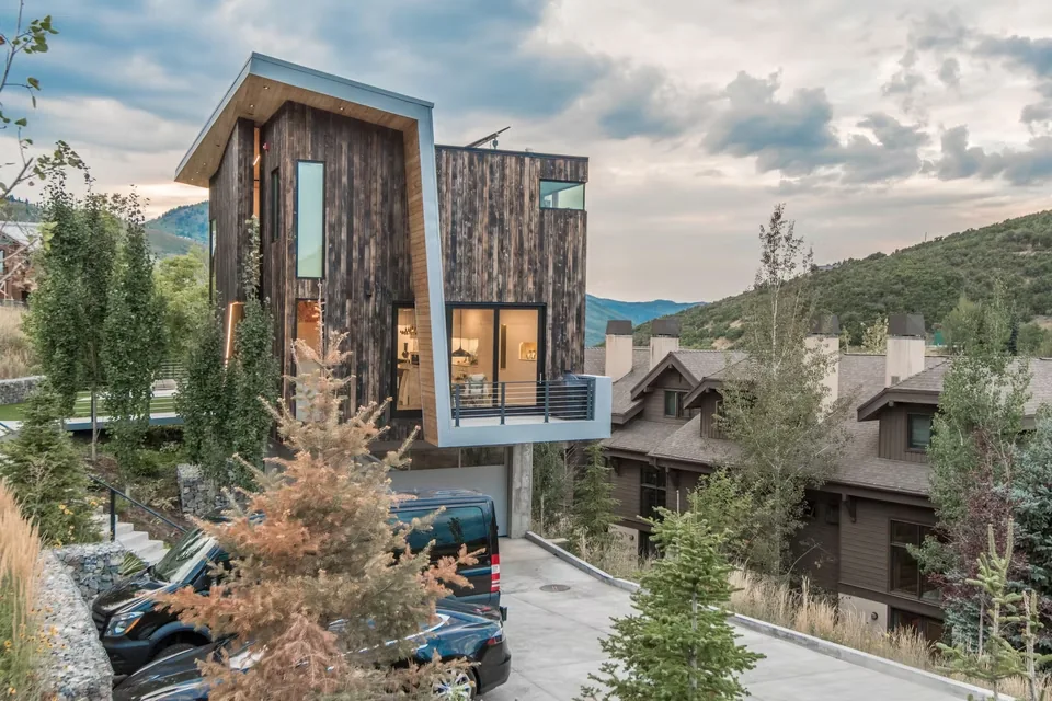 Exterior front view of a modern wood-clad house with a flat roof and cantilevered balcony.