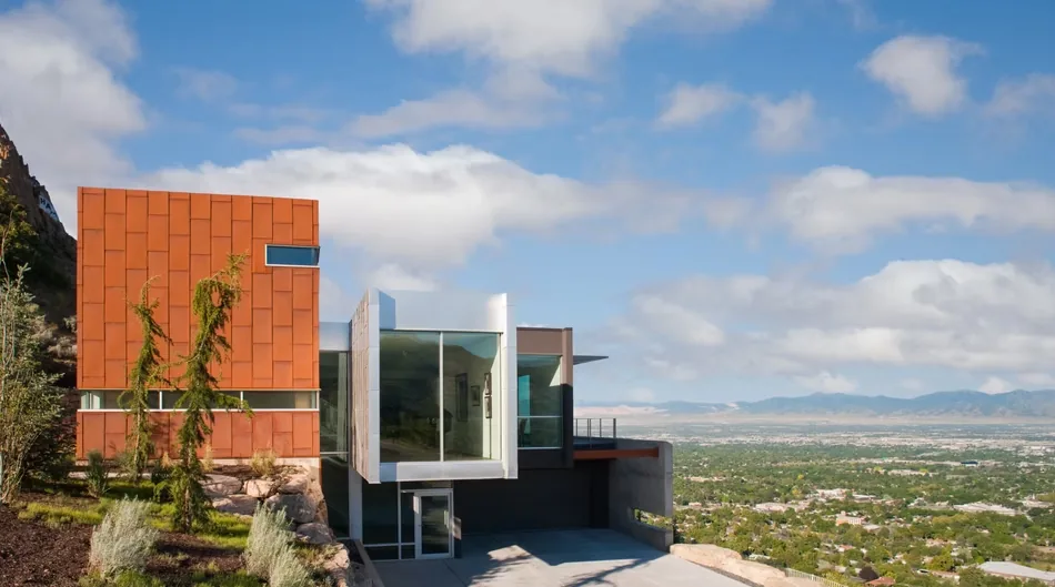 Exterior front view of a modern house with a cantilevered glass volume and rusty metal cladding on a hillside.