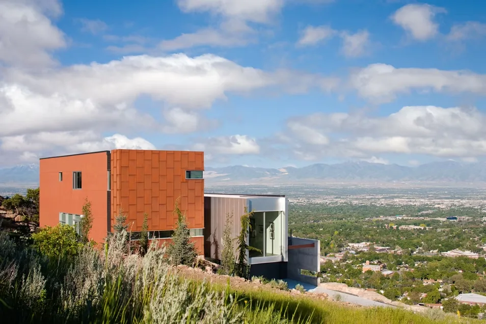 Modern house on a rocky site with flat roof and mixed material cladding including corten steel and glass.