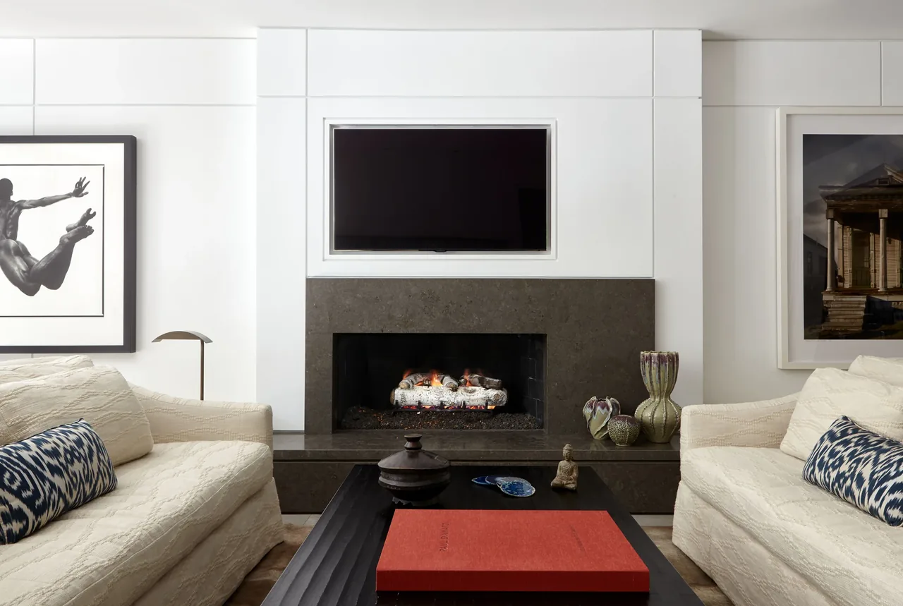 Living room featuring a fireplace with dark stone surround and mounted TV above, flanked by two cream sofas and accented with artwork.