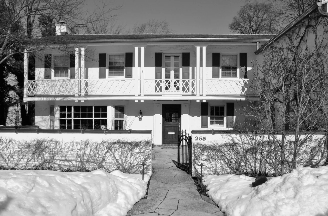 Front elevation of a two-story residence showing a balcony with crisscross railing and shuttered windows.