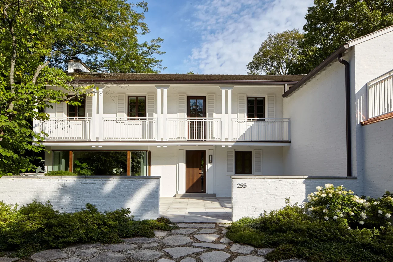 Front exterior view of the Glencoe Residence featuring a gable roof, shuttered windows, white balcony railing, and a wooden front door.