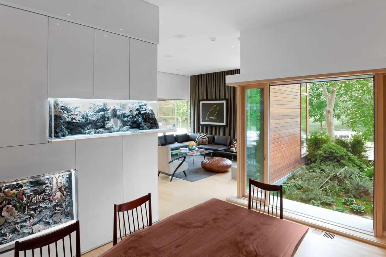 Interior view showing the dining area with built-in aquariums, large window to courtyard, and living room with seating and artwork.