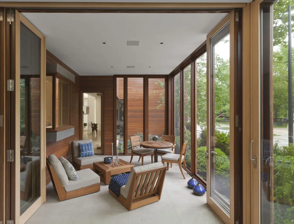 Enclosed patio with floor-to-ceiling glazing and wood furniture.