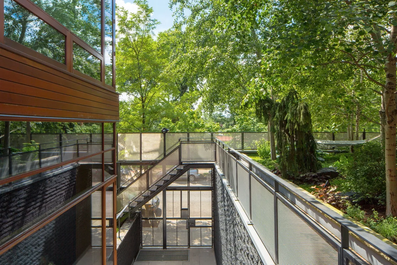 Exterior passage with metal stair and glass facade on a building with horizontal wood siding and flat roof, adjacent to planted landscape.