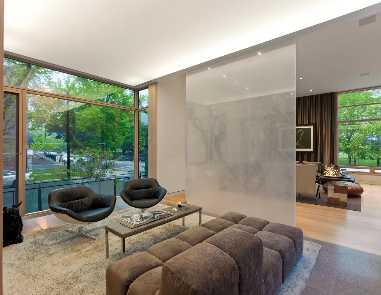 Modern living room with corner floor-to-ceiling windows, plush seating, and minimalistic furnishings.
