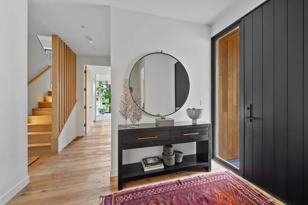 Entry space featuring a black vertical panel door and console table with a round mirror, adjacent to a stair with wood railing.