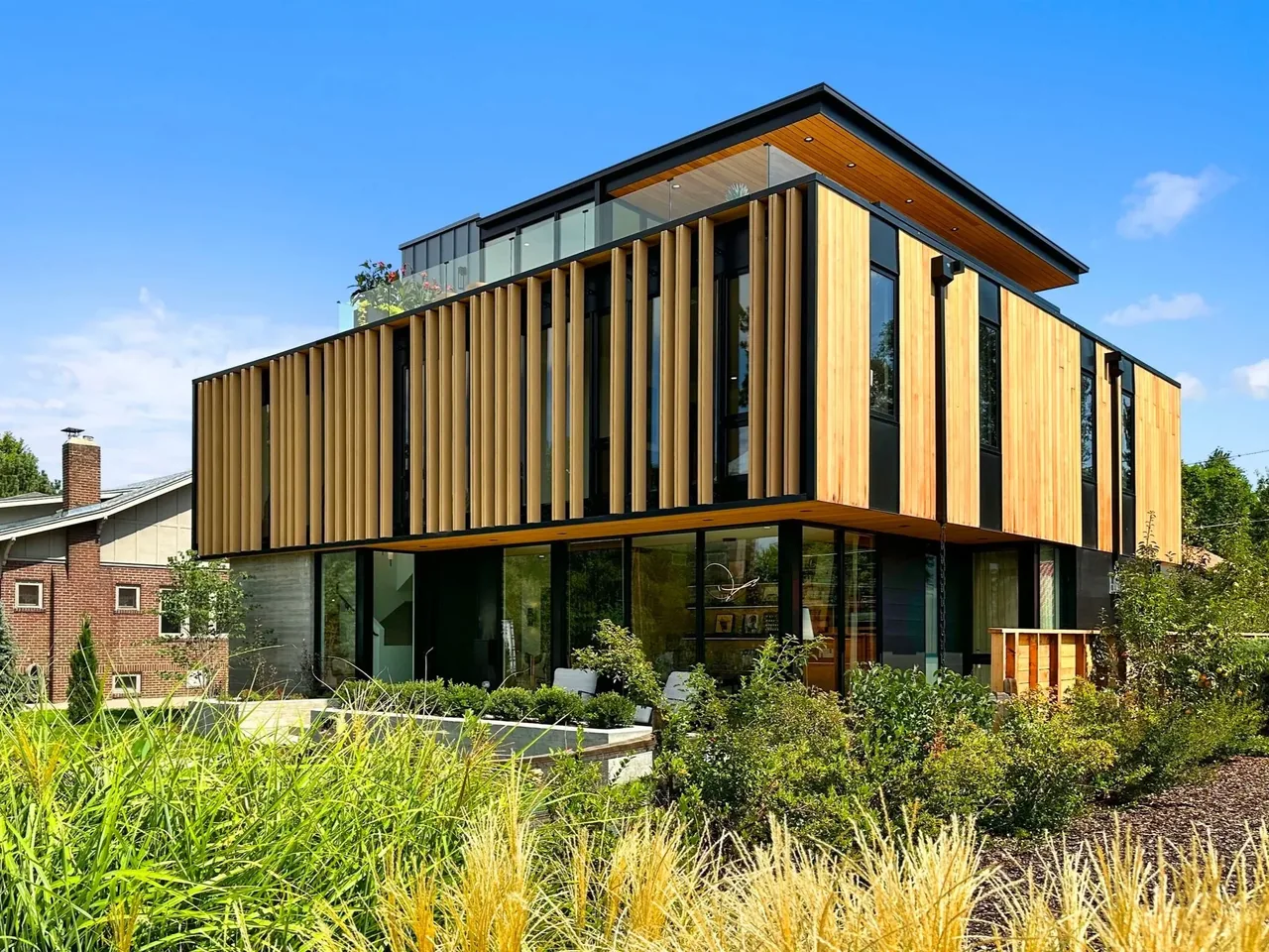 Modern house exterior featuring vertical wood louvers, floor-to-ceiling glazing, and a flat roof with a rooftop terrace.