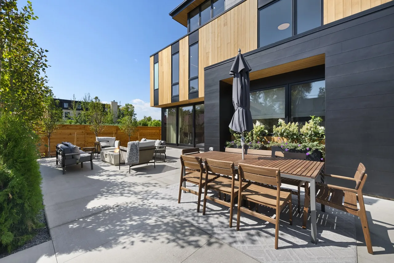 Patio exterior of a modern house featuring wood and dark paneling with outdoor dining and seating areas.