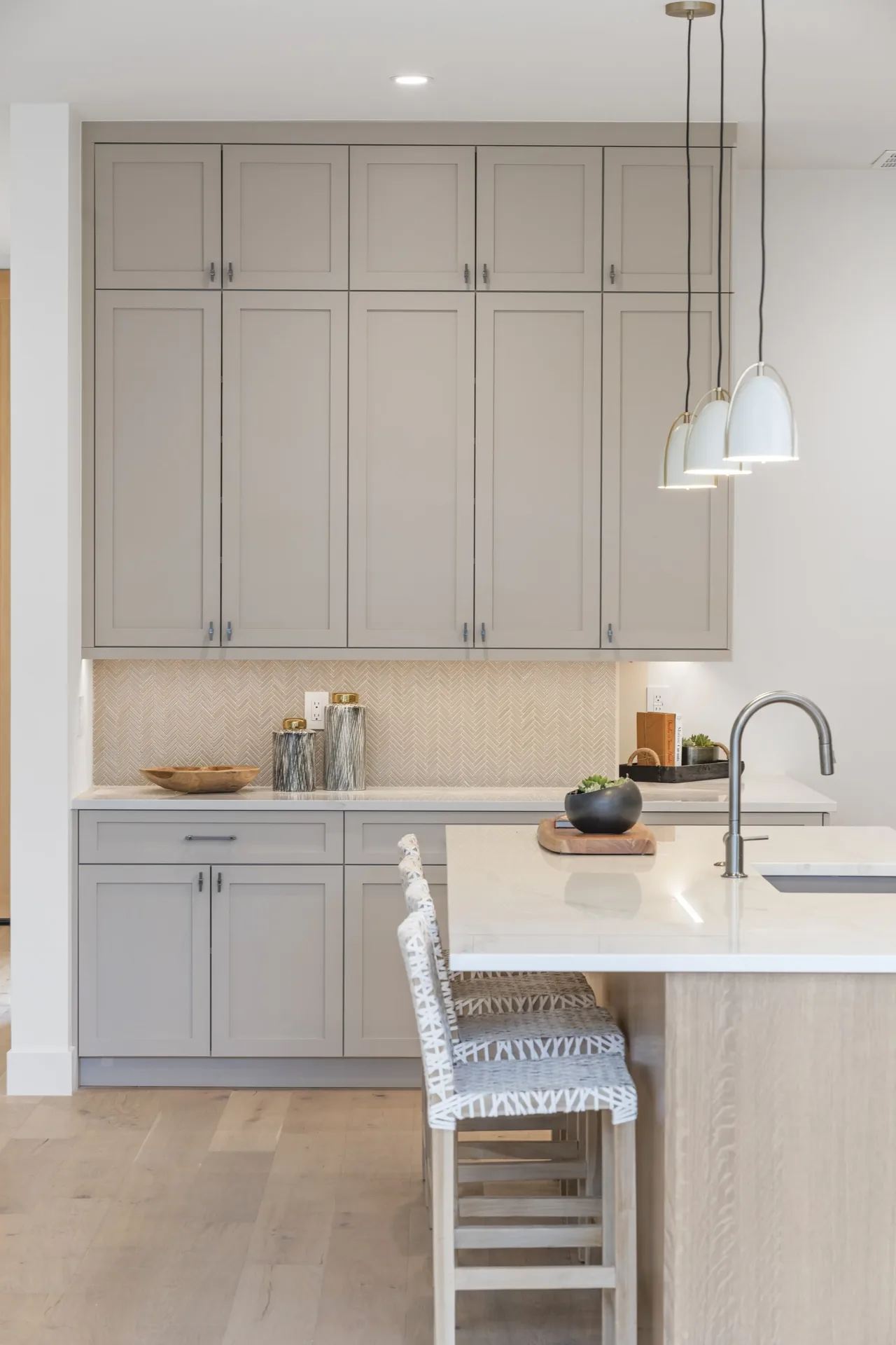 Kitchen features beige cabinetry and a white island countertop with pendant lighting and woven bar stools.