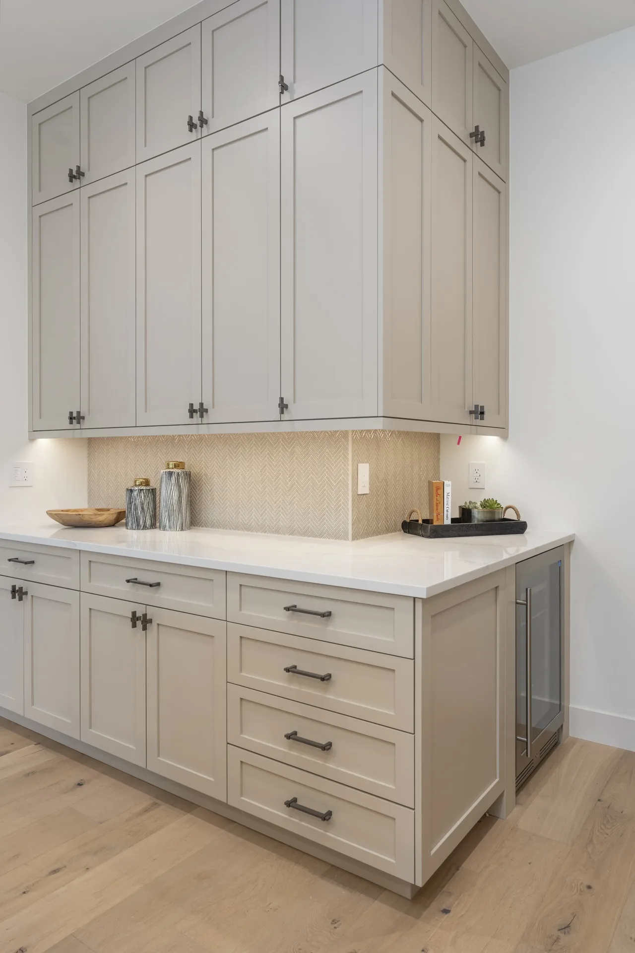 Kitchen cabinetry with light gray Shaker-style cabinets, white countertop, and herringbone tile backsplash at Wash Park 2 project.