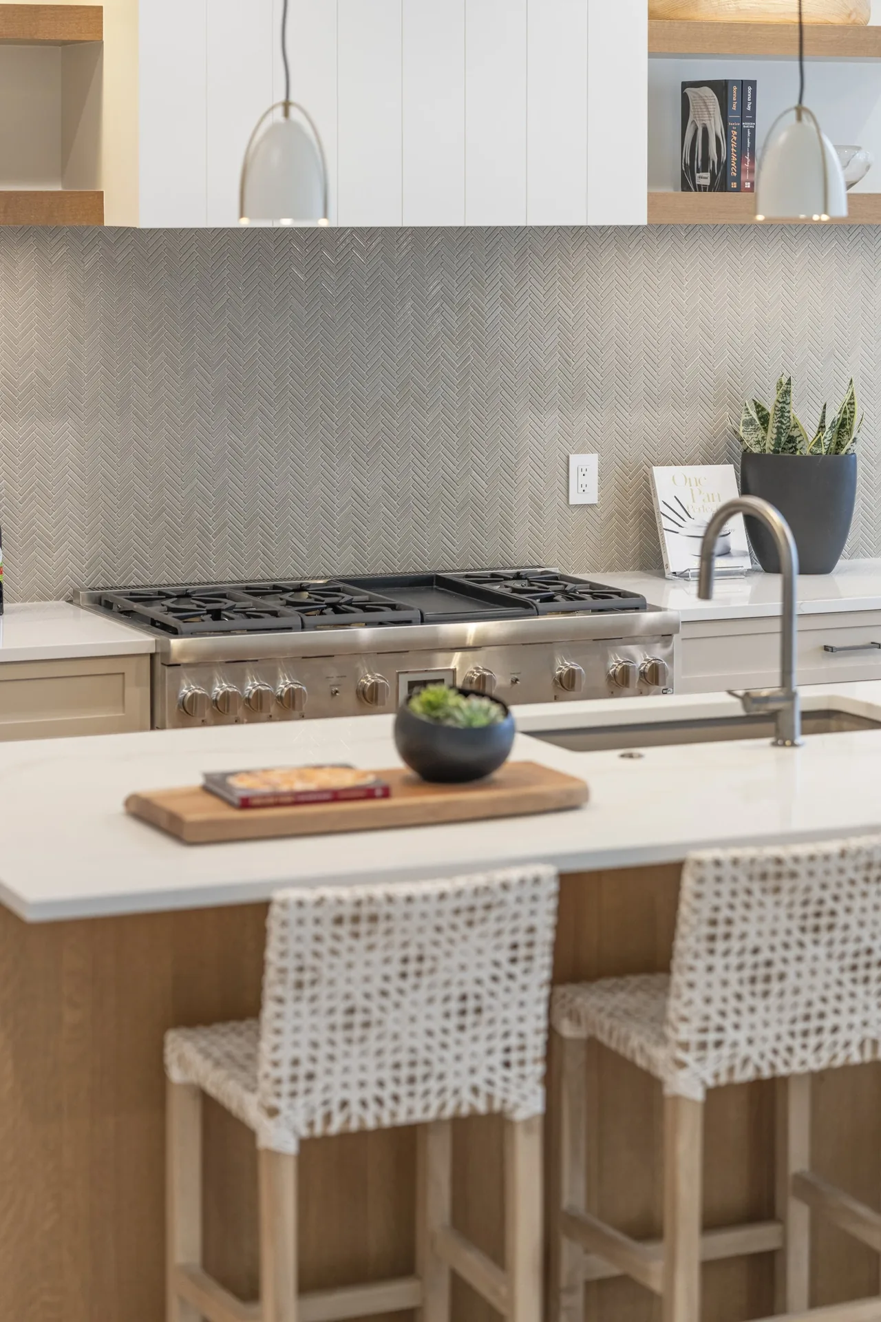 Kitchen features a stainless steel gas cooktop and oven, white cabinetry, textured tile backsplash, and a breakfast bar with woven seating.
