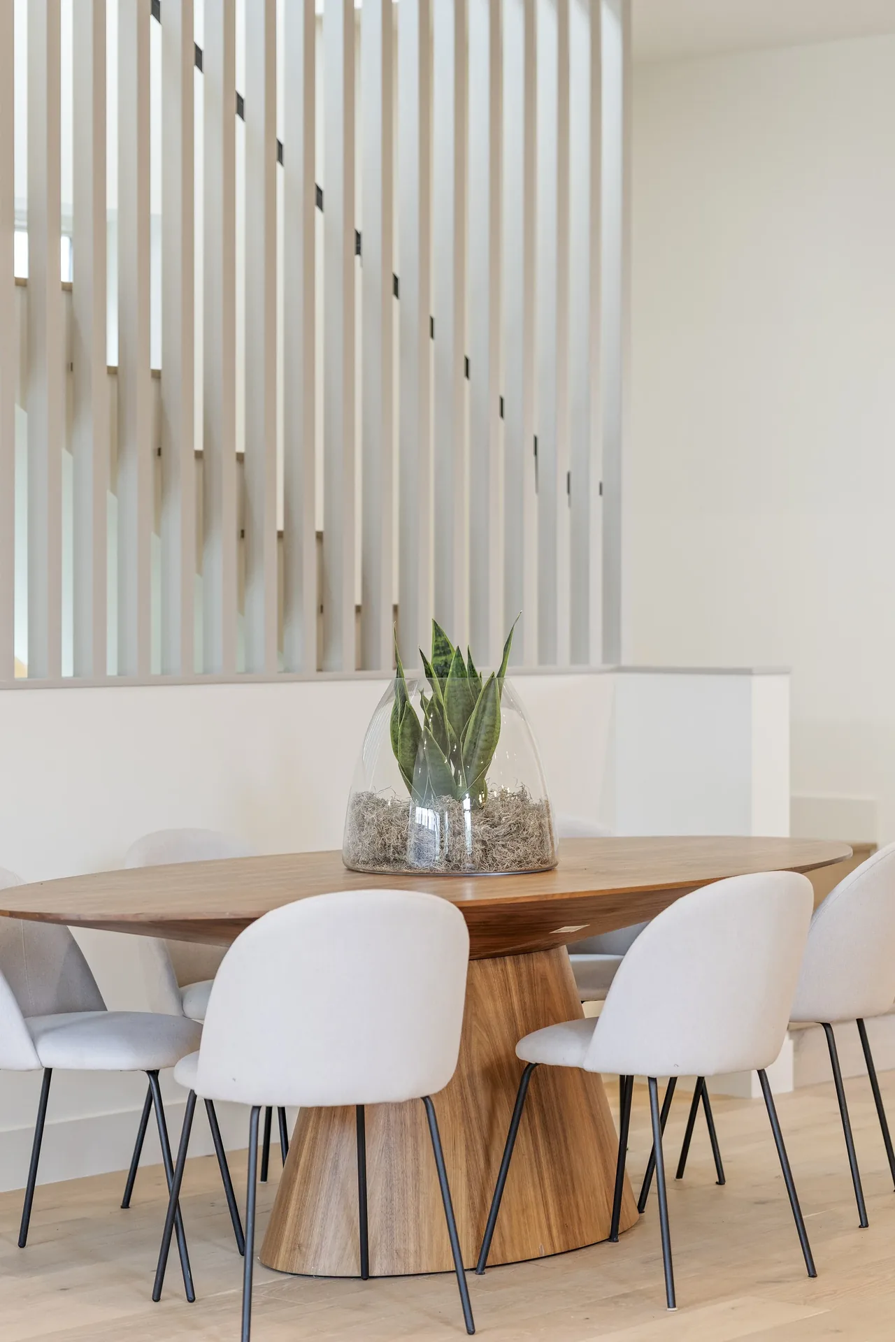 Dining area features an oval wood table with six white upholstered chairs and a glass terrarium centerpiece.