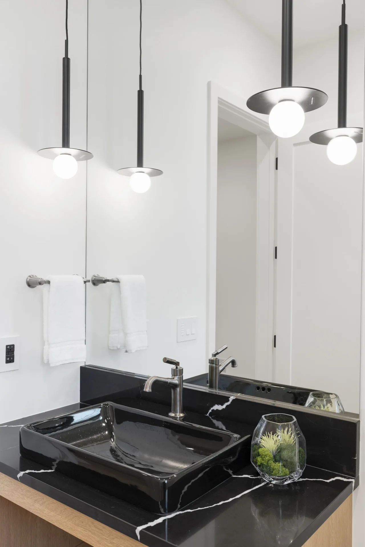 Modern bathroom sink area features a black rectangular vessel sink with matching black countertop and two hanging cylindrical pendant lights.